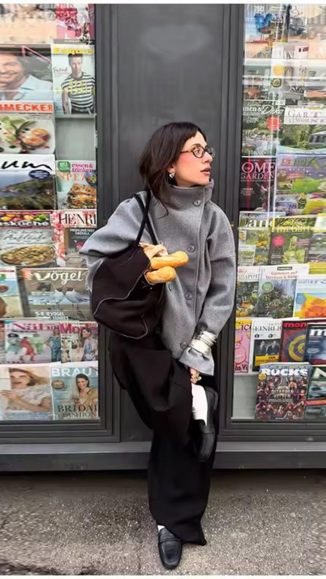 Person wearing a gray coat and black pants standing in front of a magazine rack.