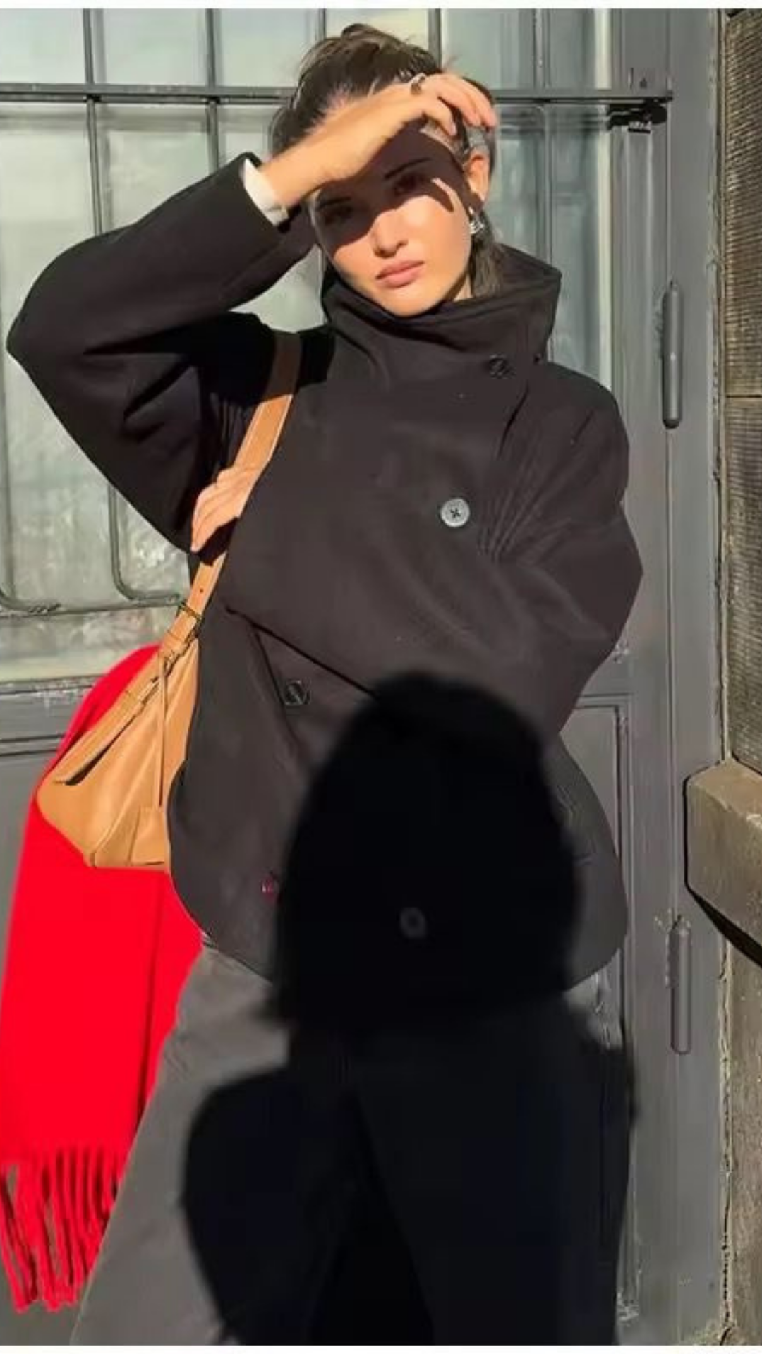 Person wearing a dark coat with a red scarf, standing in front of a glass door.