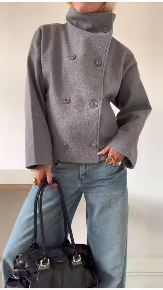 Person wearing a gray coat with a high collar and blue jeans, holding a black handbag.